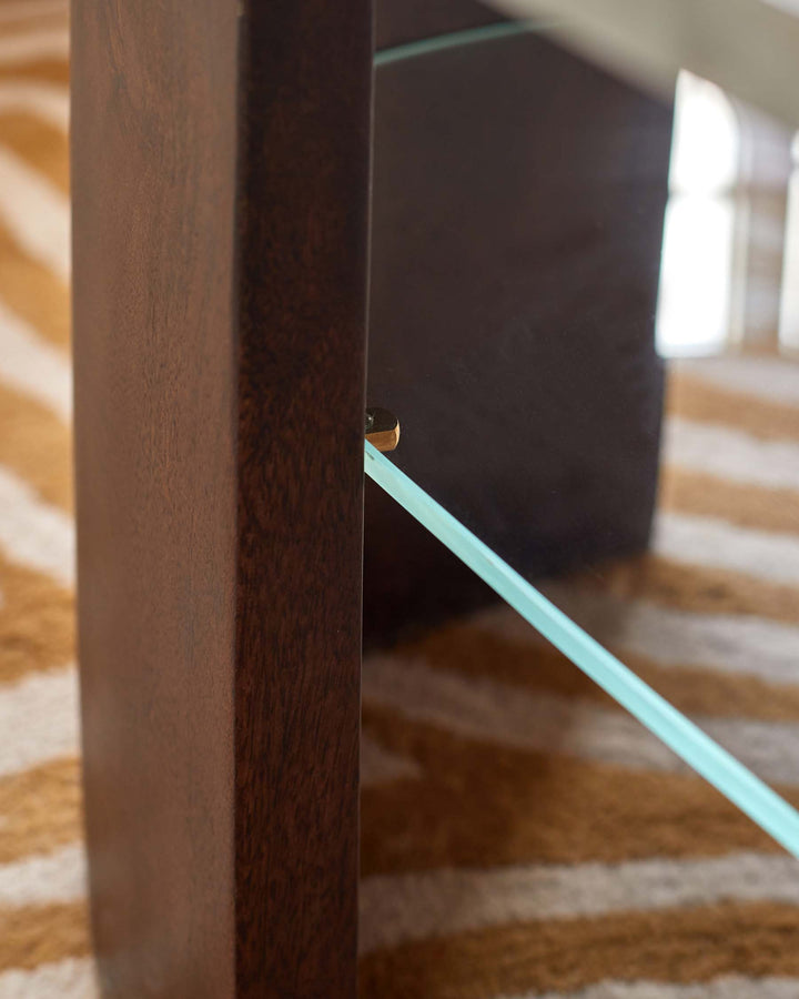Close-up of a dark wood and glass furniture piece, showcasing craftsmanship and modern design, set against a striped rug.