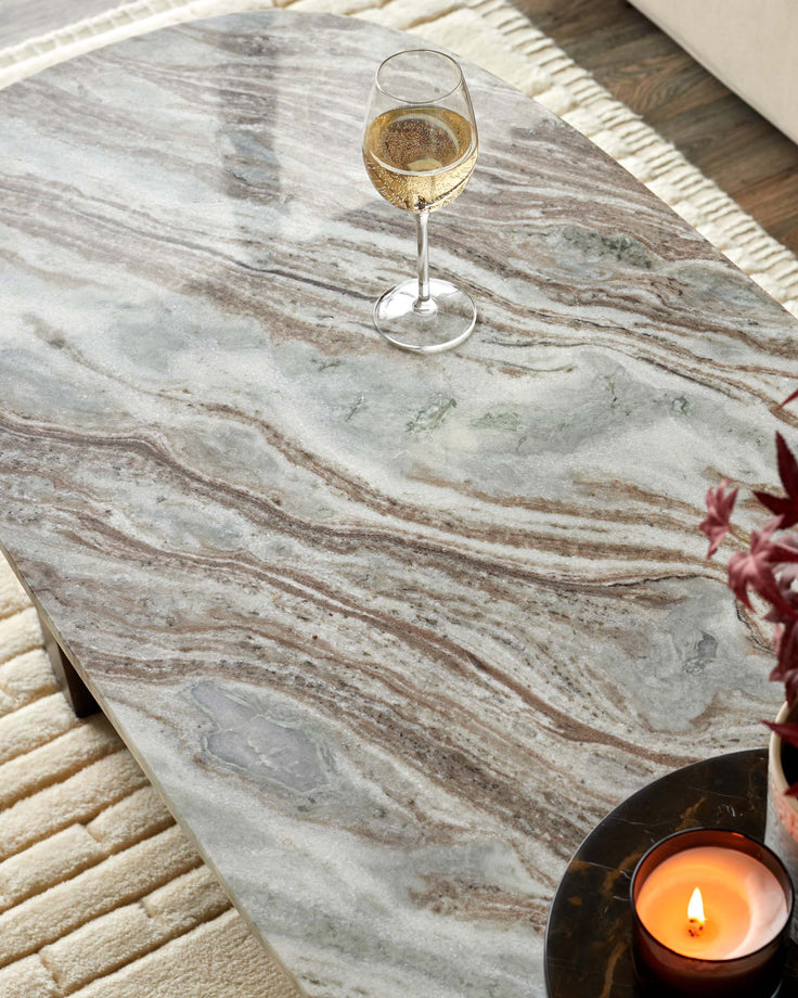 A grey marble-topped coffee table with a glass of fizz on it, alongside a lit candle and a neutral rug.