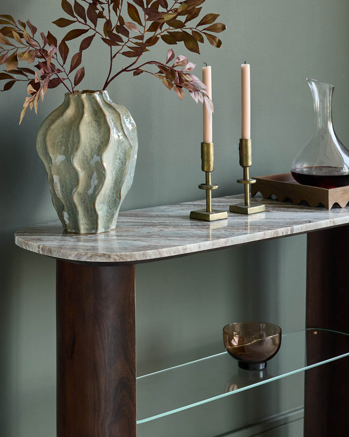 Adalynn console table in dark wood with white marble top, styled with dried florals, brass candlesticks, and decorative objects.