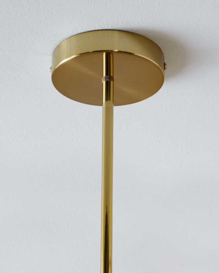 A brass pendant light fitting affixed to a white ceiling with a long stem.