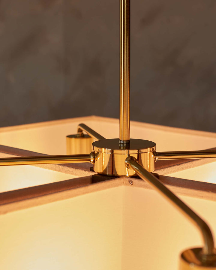 Close-up of a brass chandelier, showing the central column and radiating arms, with a square lampshade, casting warm light.