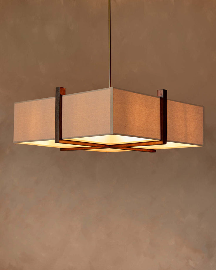 A square, beige fabric shade chandelier with a dark wood frame, hanging from a golden rod.