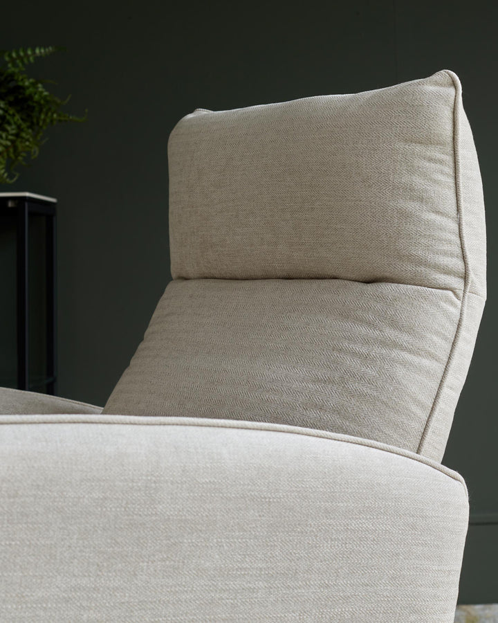 Close-up of a comfy, light-coloured upholstered armchair with a high back against a dark green wall. Modern design.