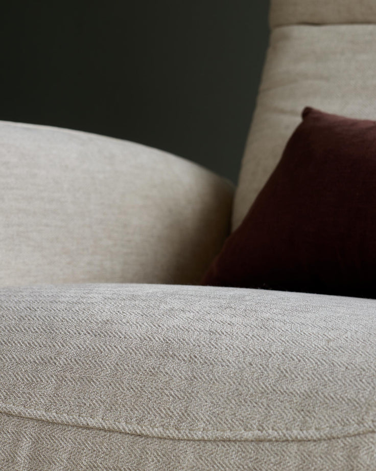 A close-up of a beige sofa with a textured herringbone pattern, and a brown cushion.