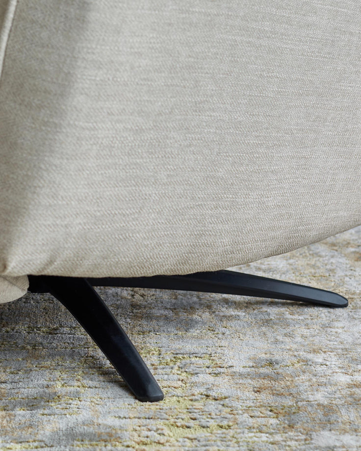 A close up of a chair's legs and upholstery. The chair is beige, and the legs are black metal.