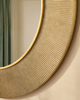 Gold round wall mirror with ribbed texture detail and curved gold frame, mounted on beige wall.
