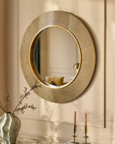 Gold round wall mirror with textured radial pattern frame, displayed above marble surface with candles and dried flowers.