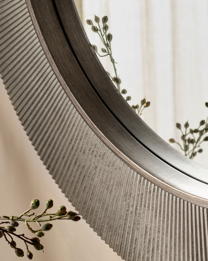 Round silver wall mirror with ribbed textured frame, displayed at an angle with dried botanicals.