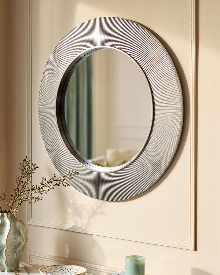 Round silver wall mirror with textured rippled frame, displayed above a console table with decorative vase and accessories.