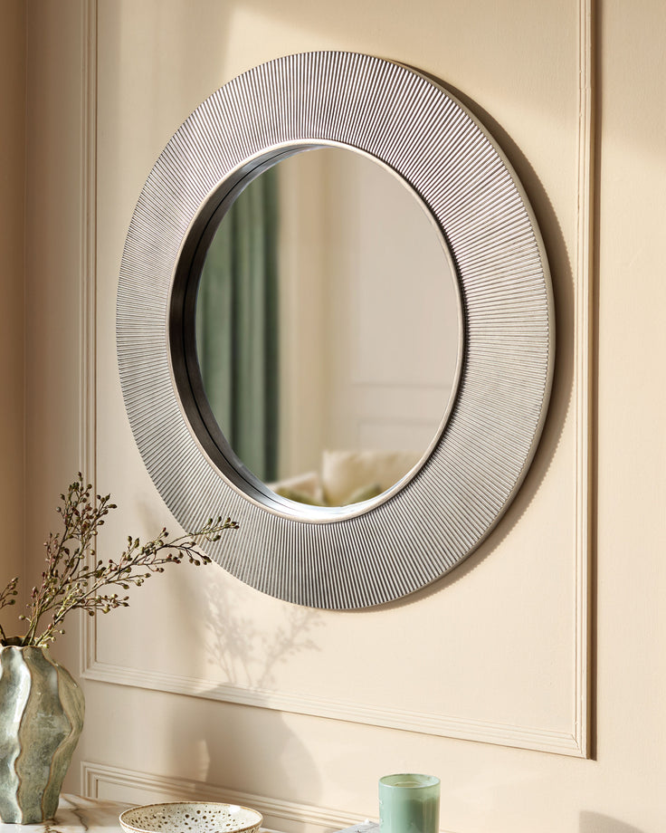 Round silver wall mirror with textured rippled frame, displayed above a console table with decorative vase and accessories.