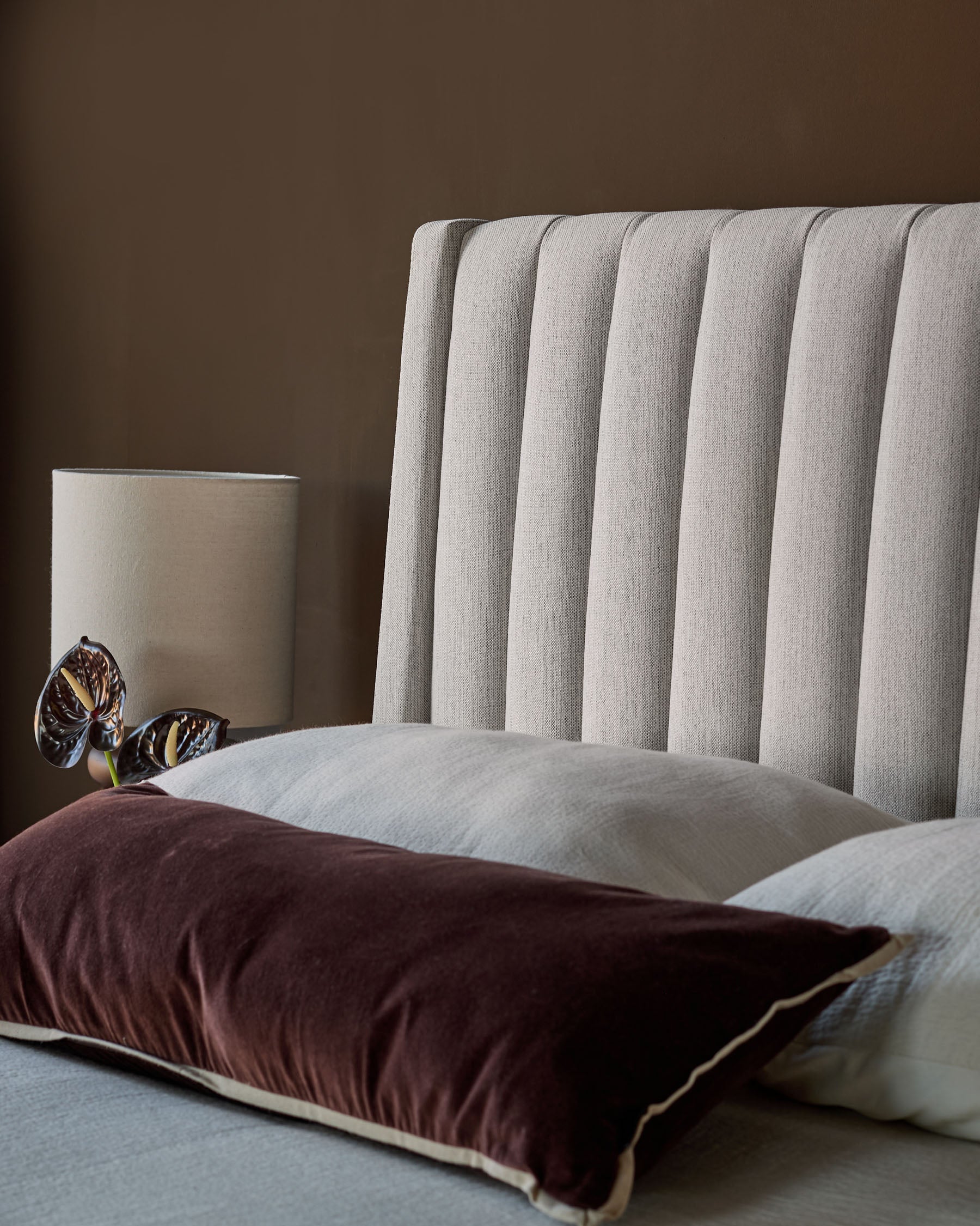 Amalfi fabric double bed with ivory upholstered headboard featuring vertical channel quilting, styled with burgundy and cream pillows.