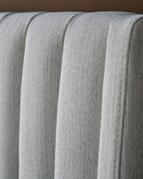 Ivory fabric bed with vertical channel quilting detail, close-up showing textured upholstery and plush stitched design.