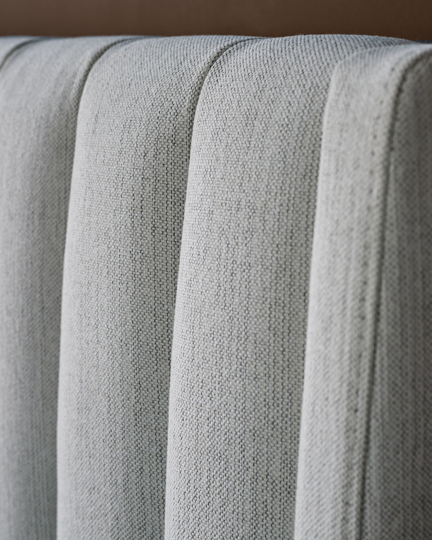 Ivory fabric bed with vertical channel quilting detail, close-up showing textured upholstery and plush stitched design.