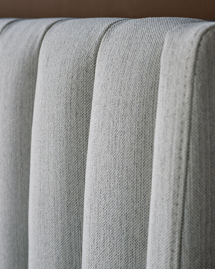 Ivory fabric bed with vertical channel quilting detail, close-up showing textured upholstery and plush stitched design.
