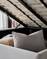 Ivory fabric double bed with storage, showing plush pillows and open wooden slat headboard with black frame detail.