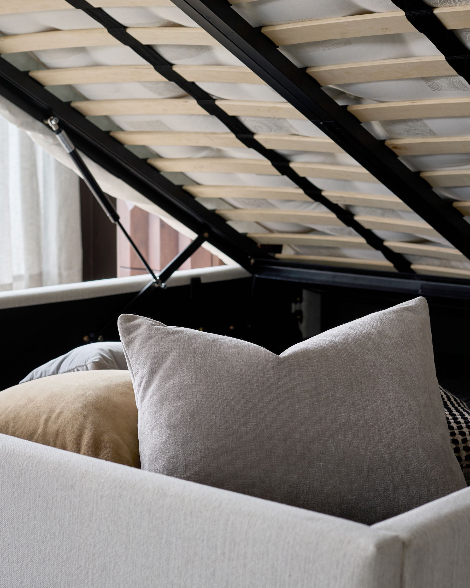 Ivory fabric double bed with storage, showing plush pillows and open wooden slat headboard with black frame detail.