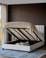 Ivory fabric double bed with open storage compartment, showing wooden slat base and beige throw blanket.