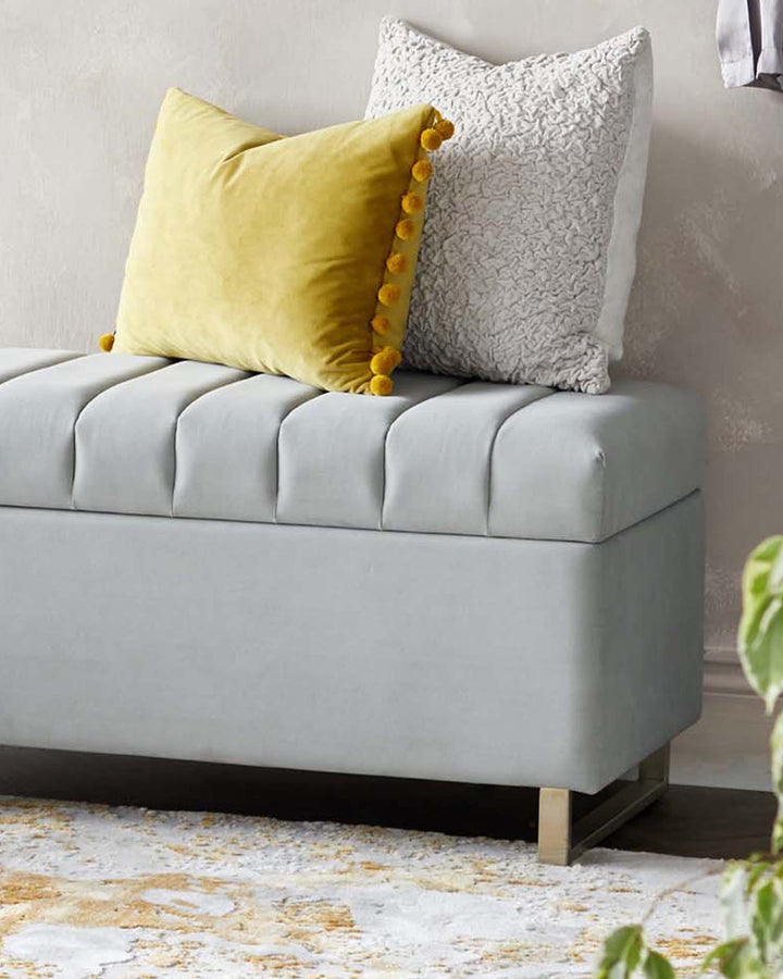 Amalfi light grey velvet ottoman bench with channel quilting, styled with yellow and grey throw pillows.