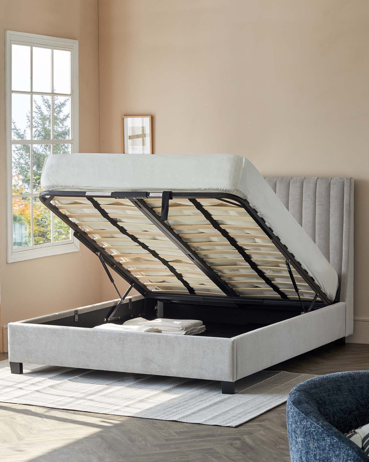 Upholstered light grey storage bed with a tufted headboard and a lifted mattress platform revealing an open storage compartment.