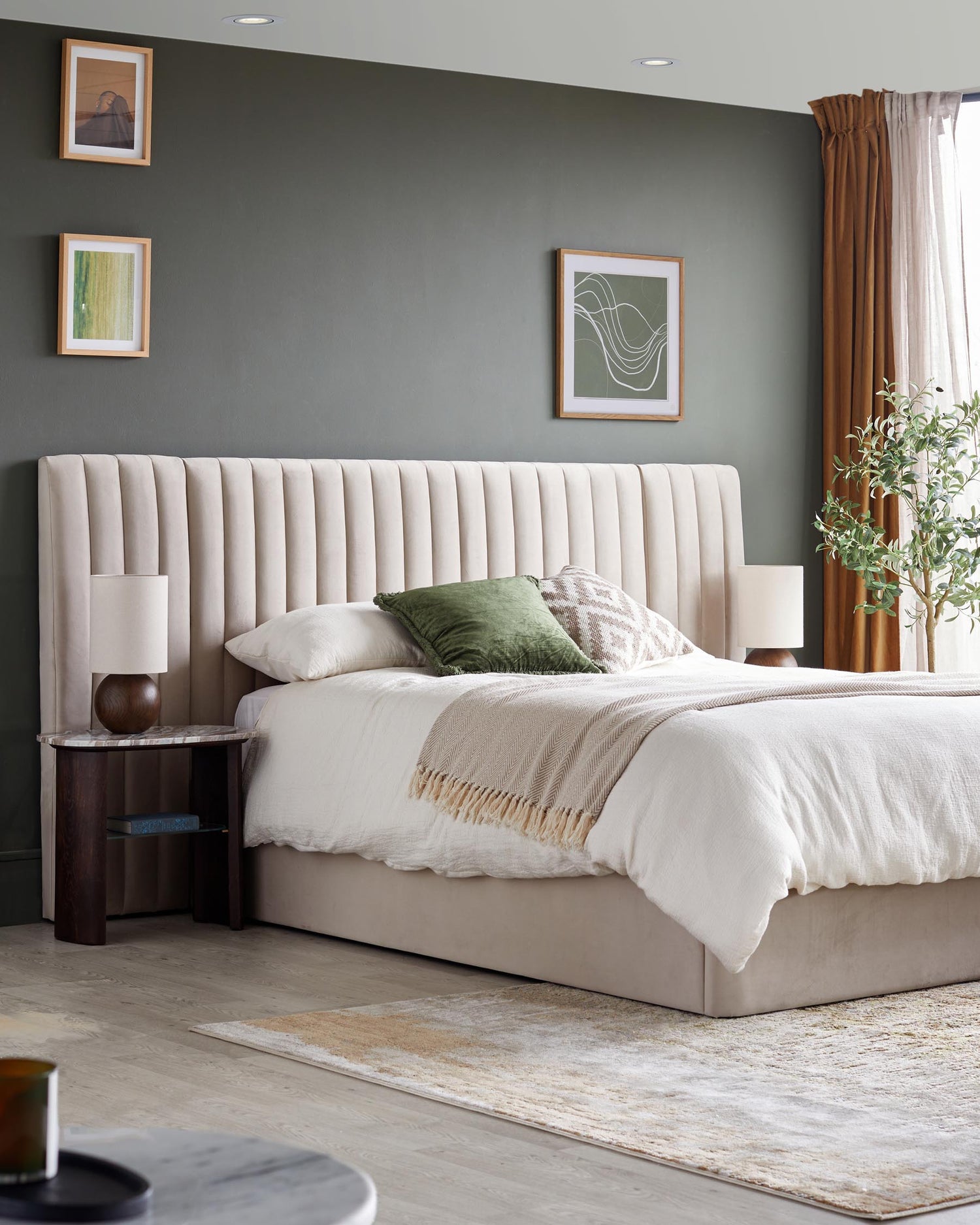 Bedroom with beige, ridged headboard bed, bedside table, olive tree and warm coloured accents.