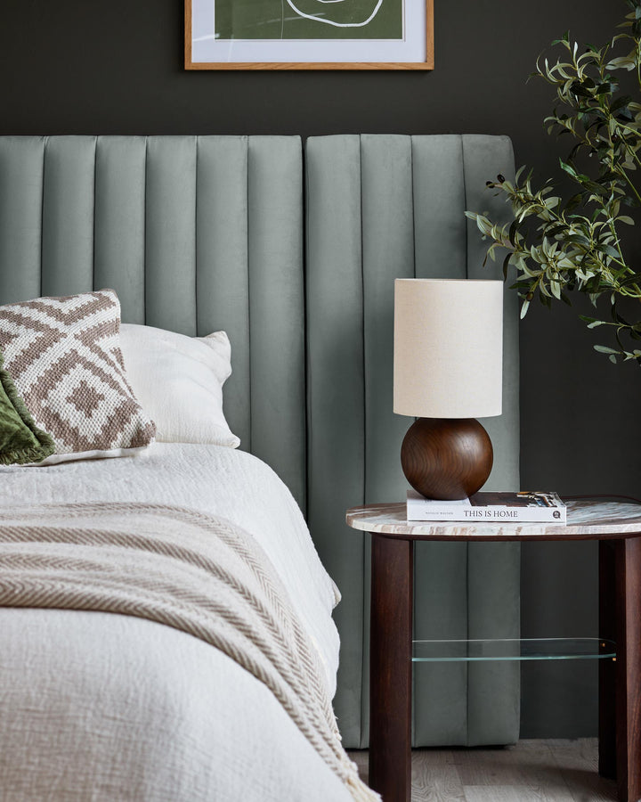 Bedroom with upholstered headboard, side table with lamp and decorative plant. Stylish and inviting bedroom.