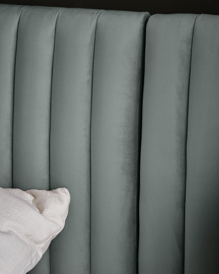 Close-up of a light blue upholstered headboard with vertical channel tufting and a white pillow.