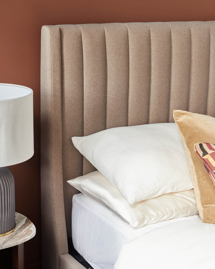 A stylish bedroom setup featuring a fluted headboard, layered pillows, and a sleek bedside table with a lamp.