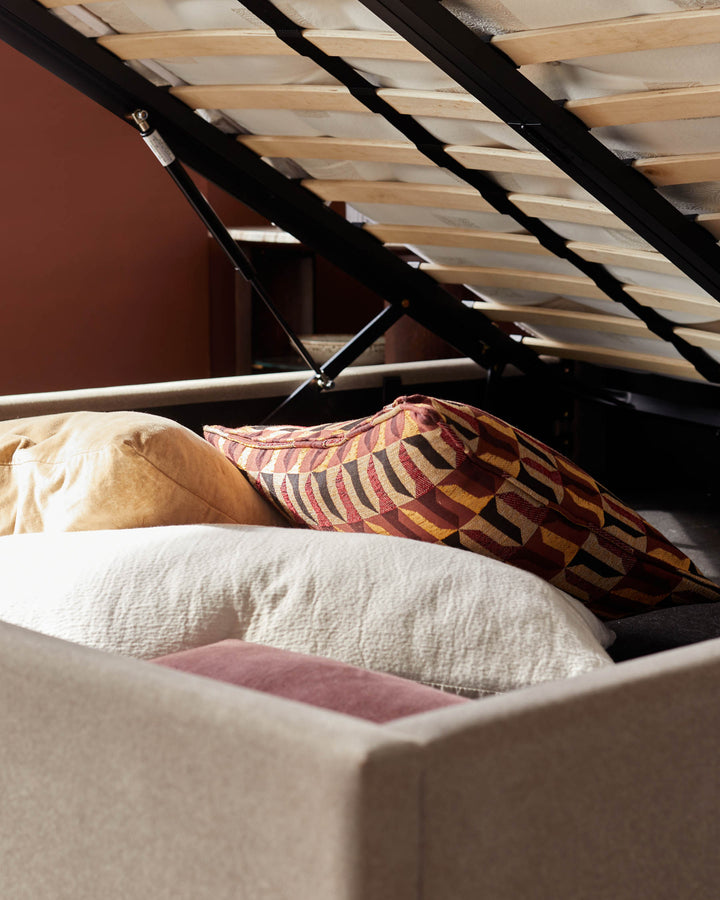 Storage bed with pillows and bedding tucked inside the lift-up base, offering space-saving functionality and style.