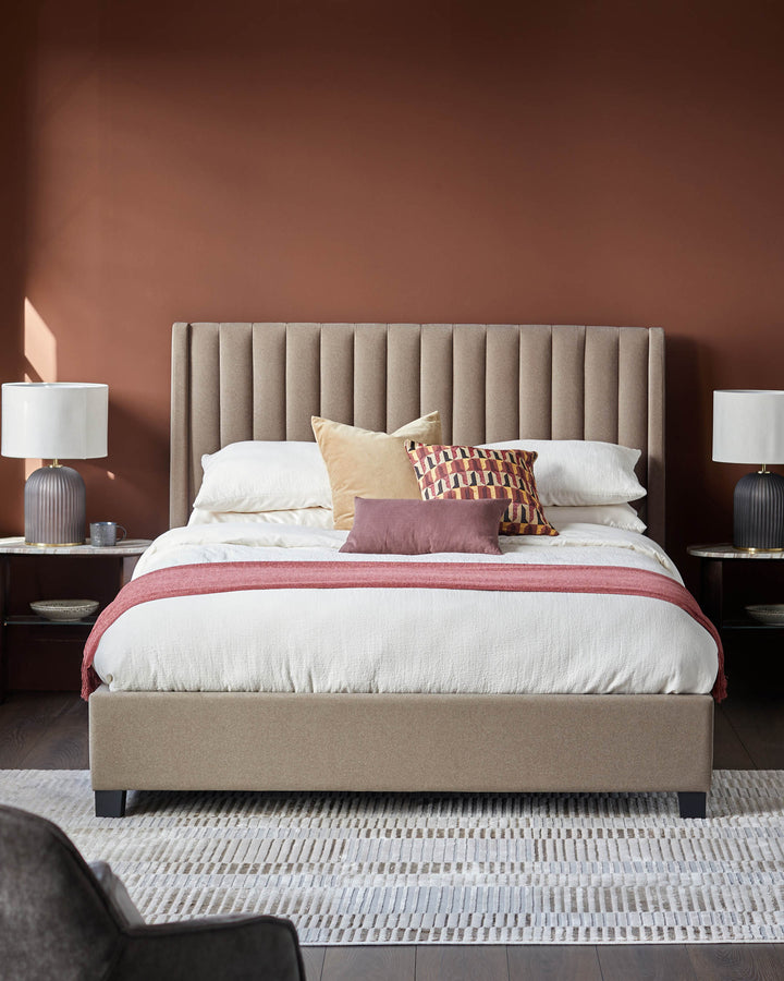 Bedroom scene with upholstered bed, matching bedside tables, lamps, textured rug, with a burnt orange wall in the background.
