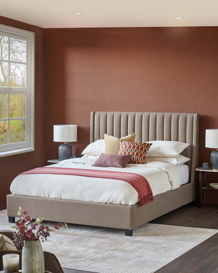 Bedroom with upholstered bed, bedside tables and lamps. A rug is partially visible. Neutral colours with a feature wall.