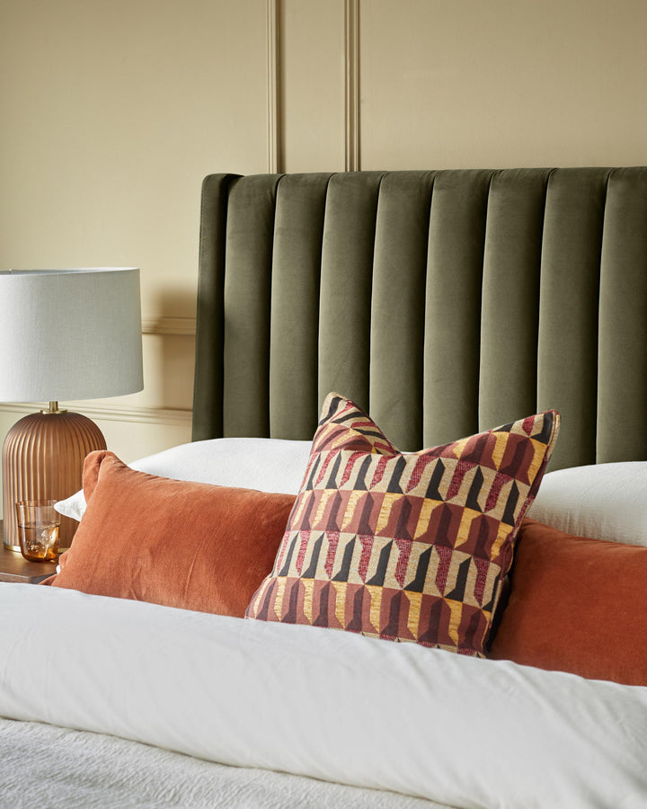 Bedroom featuring an olive green headboard, orange pillows, and geometric print cushion; neutral colour scheme.
