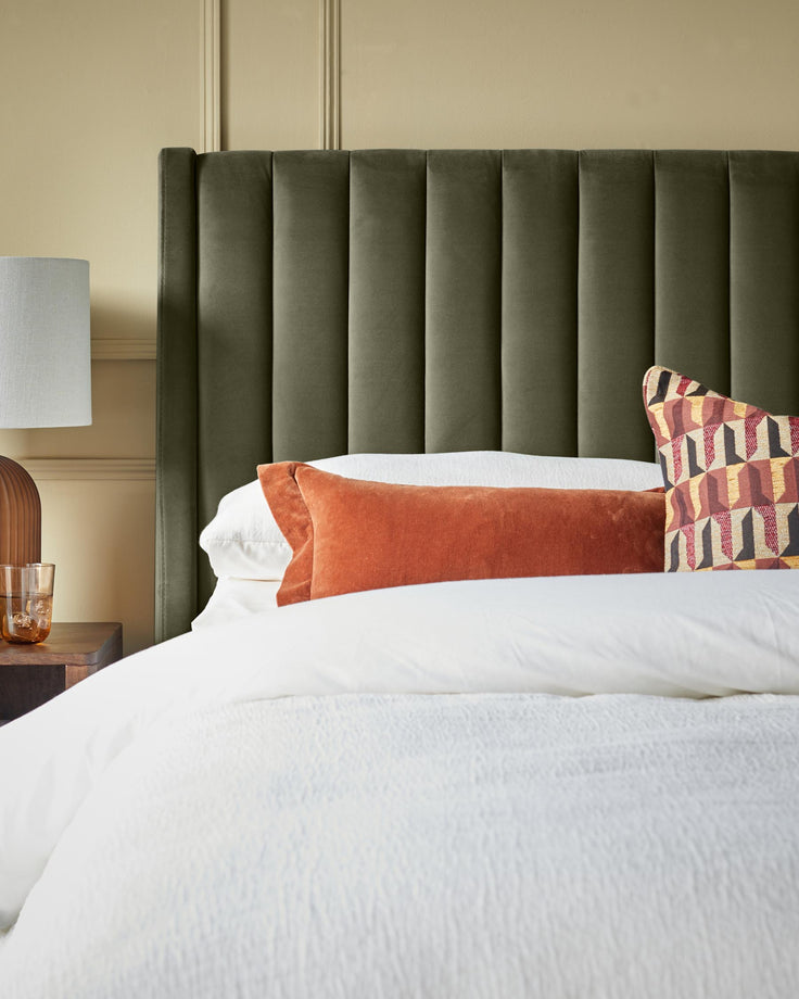 A contemporary bedroom setting with a dark green, vertically-padded headboard and textured white bedding and pillows.