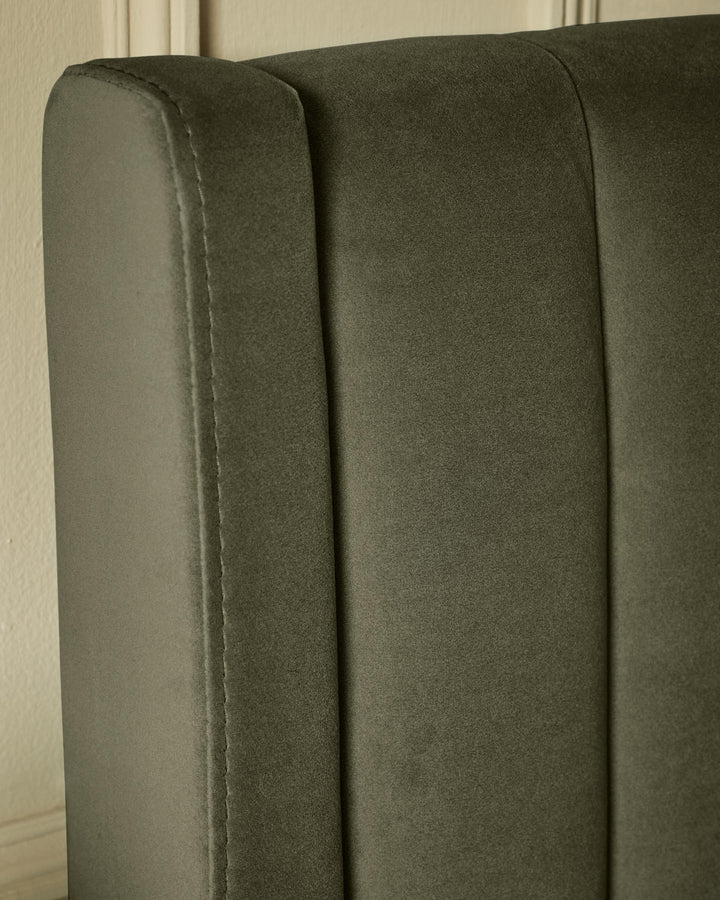 Close-up of a grey upholstered headboard featuring vertical panels and detailed stitching, adding a touch of elegance to any bedroom.