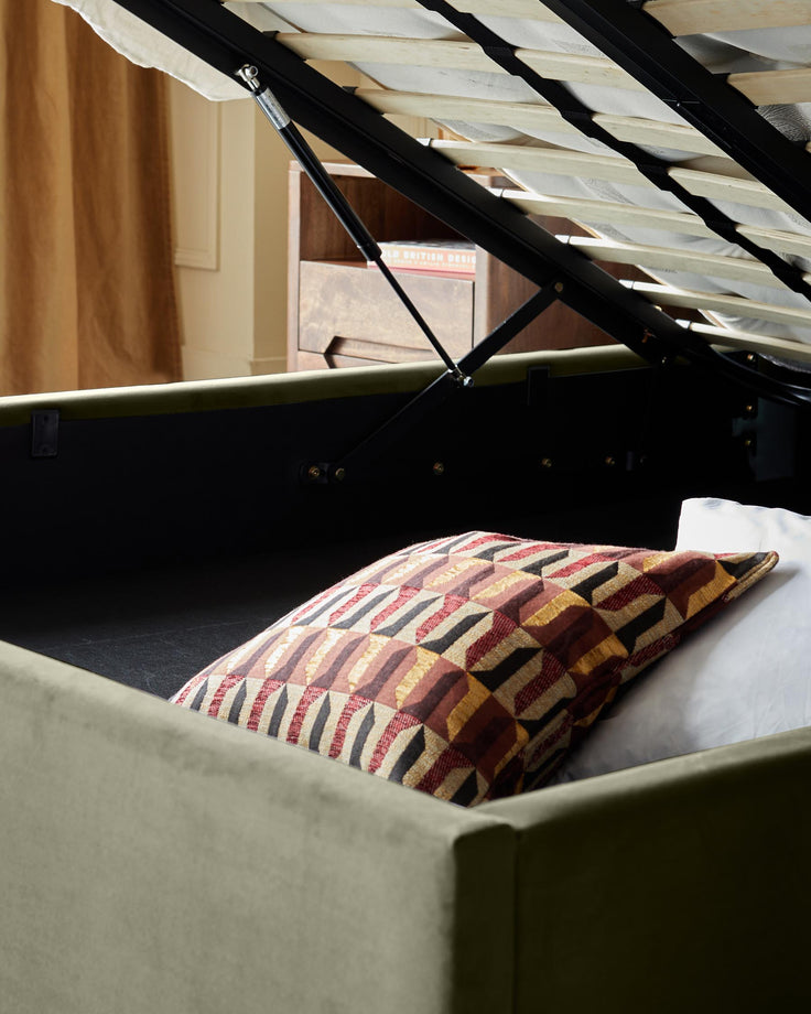 An upholstered bed with a geometric cushion and a wooden headboard shown open for storage.