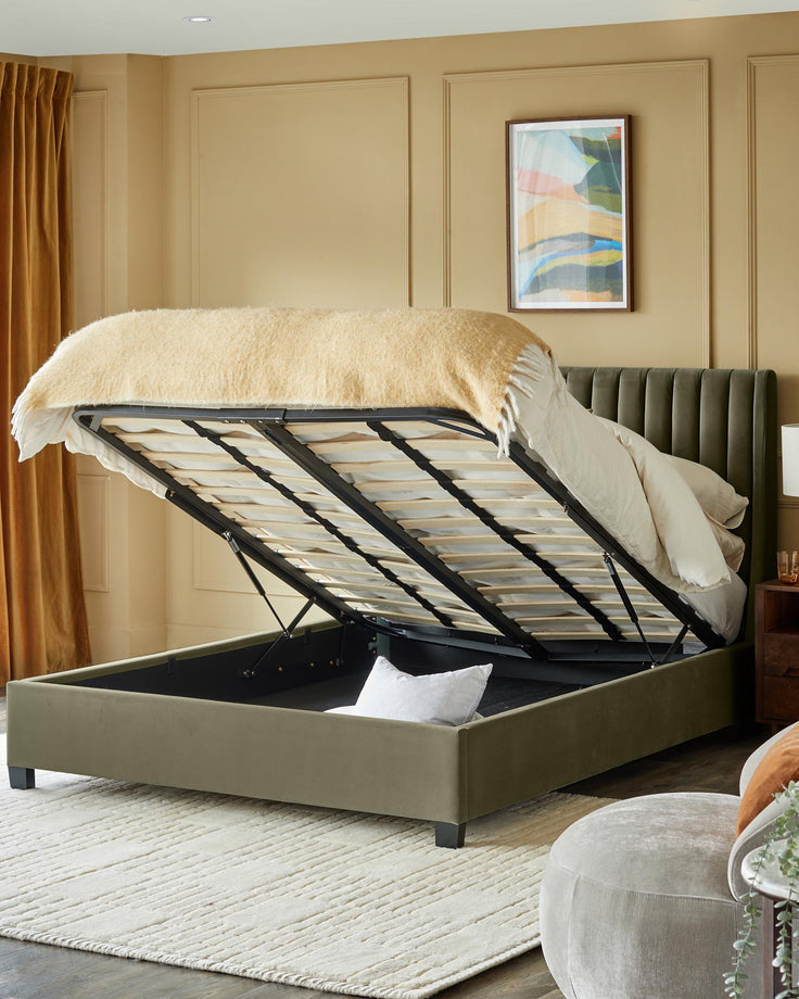 Olive green upholstered ottoman bed with lift-up base showing storage, styled with neutral bedding and a cream rug.