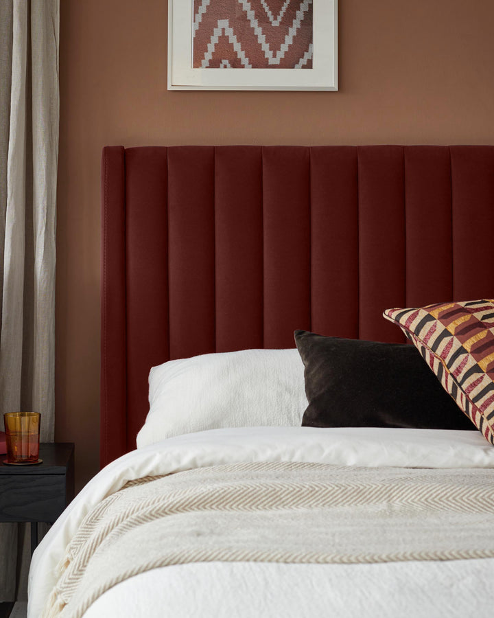 A bed with a red headboard, white bedding, and patterned pillows. A bedside table and lamp are visible.