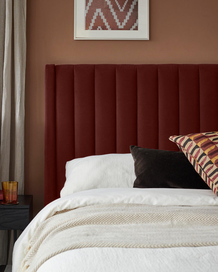 A bed with a red headboard, white bedding, and patterned pillows. A bedside table and lamp are visible.
