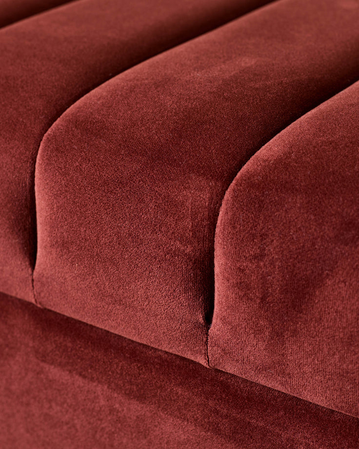 Amalfi velvet ottoman bench in toffee red, close-up detail of curved seating surface and soft fabric texture.