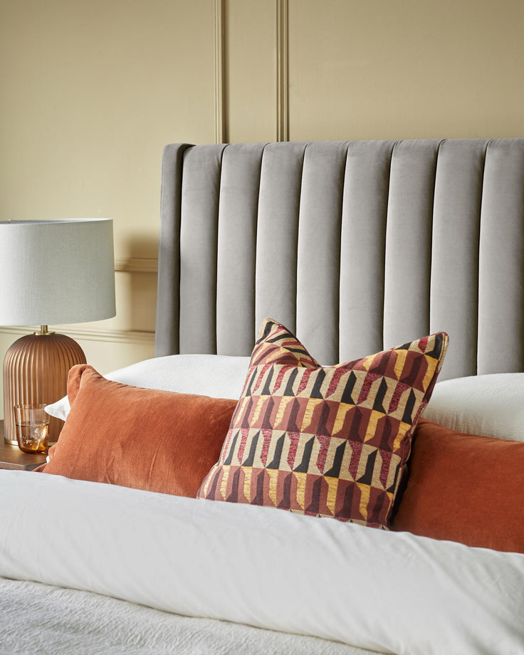Bedroom featuring a grey headboard, lamp, and decorative cushions on a bed with white bedding.