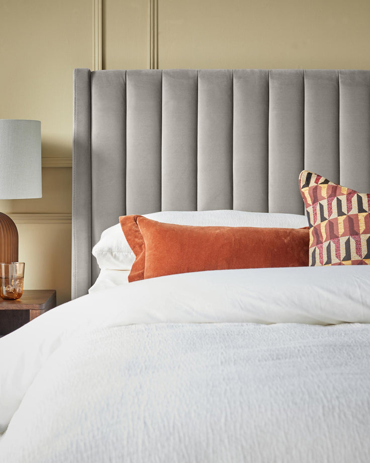 A modern bedroom featuring a grey headboard, a wooden bedside table and colourful decorative cushions.