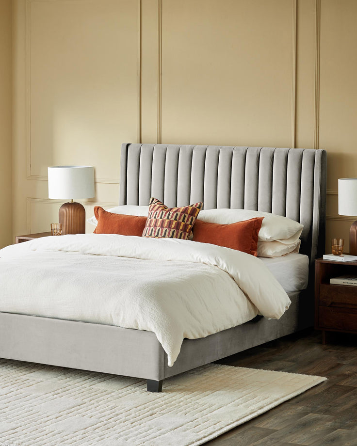 A luxurious double bed featuring a light grey, vertically-stitched headboard and rustic wooden side tables with lamps.