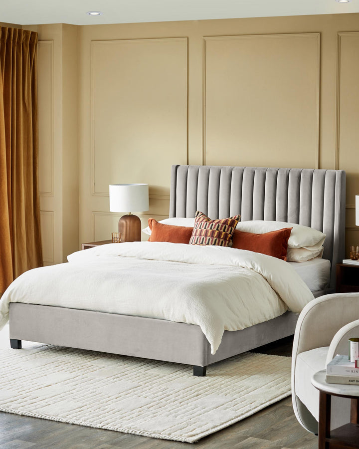 Bedroom featuring a grey velvet bed with a vertically channelled headboard, with a beige rug and side tables.
