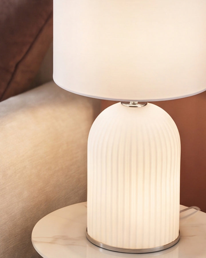 Amalfi white table lamp with ribbed ceramic base and cylindrical shade on nightstand.