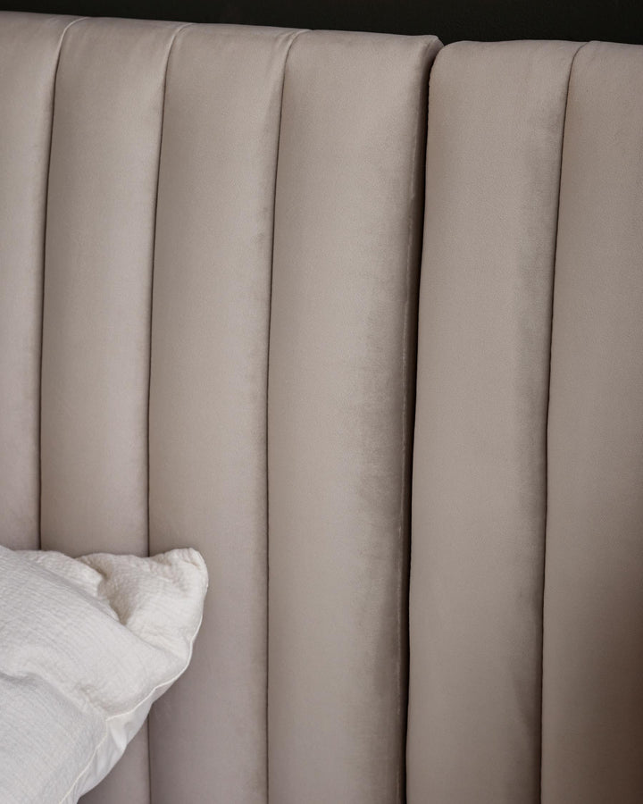 Close-up of a beige velvet headboard with vertical panelling and a white pillow, showcasing texture and elegant design.