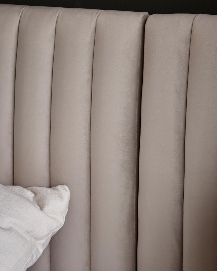 Close-up of a beige velvet headboard with vertical panelling and a white pillow, showcasing texture and elegant design.