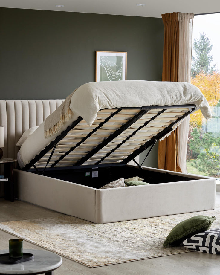 An open ottoman bed reveals storage space. Neutral tones complement the plush headboard and modern accessories.