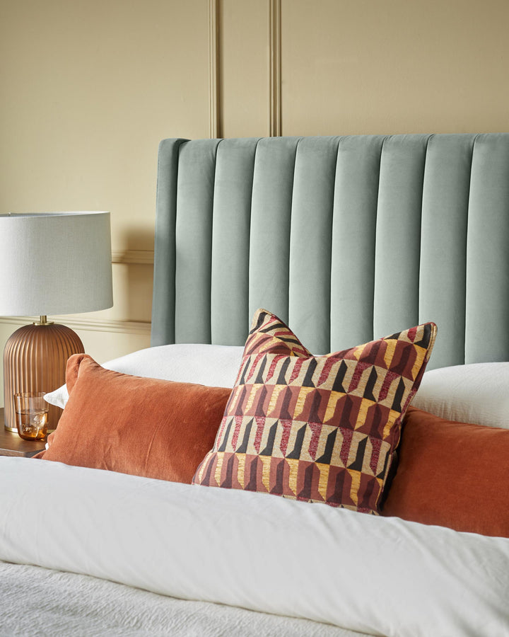Bedroom arrangement with a padded headboard, bedside table and a stylish mix of cushions on a white bedspread.