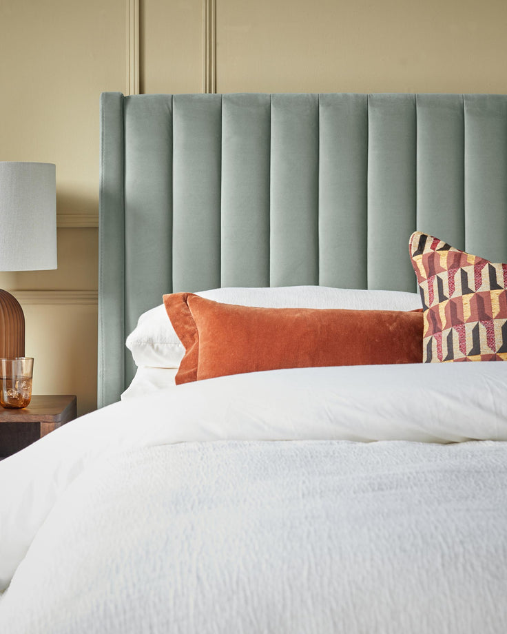 Stylish bedroom furniture. Headboard, lamp, bedside table, decorative cushions and white linen create a calming interior.