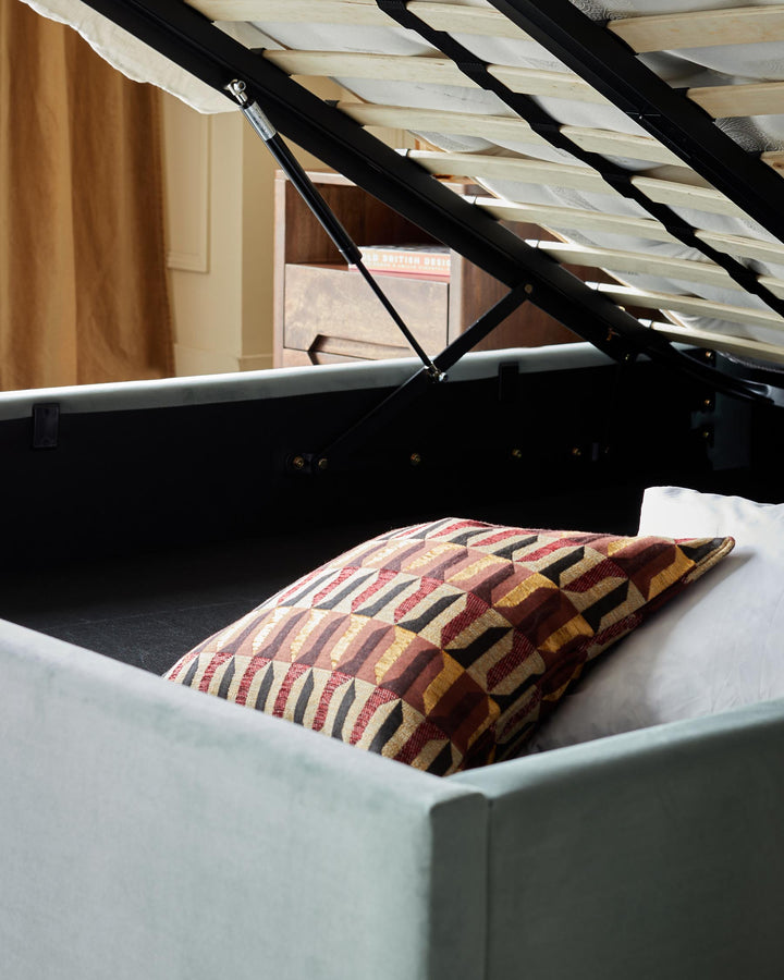 A bed with a lift-up frame, revealing storage space with cushions and bedding inside. Perfect for space-saving.