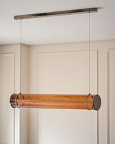 Amber glass pendant light with caramel-tinted cylindrical shade, suspended from brushed metal ceiling canopy by thin cables.